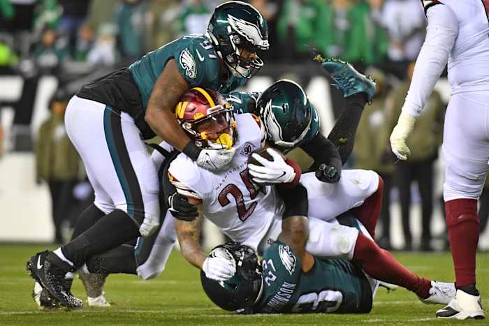 Philadelphia Eagles defenders tackle a Washington Commanders ball-carrier.